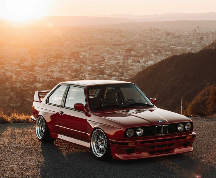 Red BMW M3 E30 overlooking a city at sunset